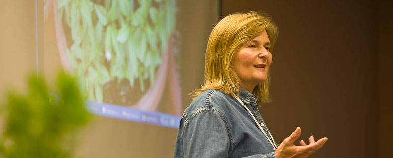 woman stands in front of projected picture of plant, speaking towards group