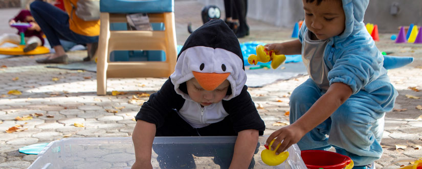 toddler in penguin onsies and toddler in blue onsie play in bucket next to each other