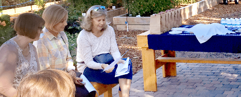 3 women on a bunch outdoors looking at a book