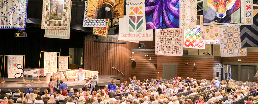 crowd in chairs with quilts hanging above