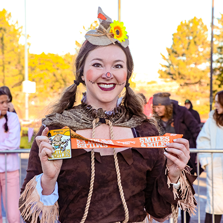 girl with scarecrow face paint and costume smiling holding medal with orange ribbon