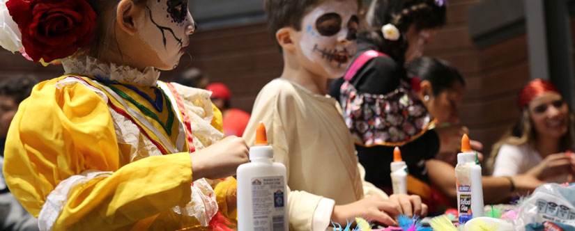 A young girl in a bright yellow dress with face paint, with glue in front of her making a craft