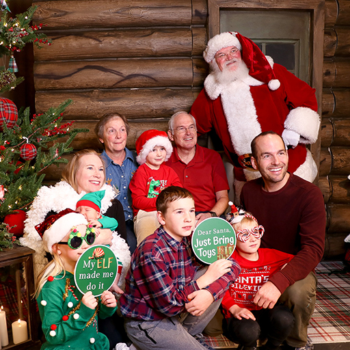 Family in red and green and santa hats, santa standing to side