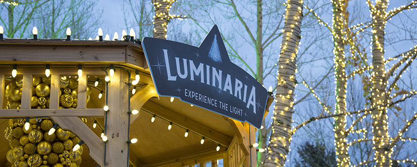 image of top roof of gazebo lit in warm yellow lights with blue Luminaria sign at front 