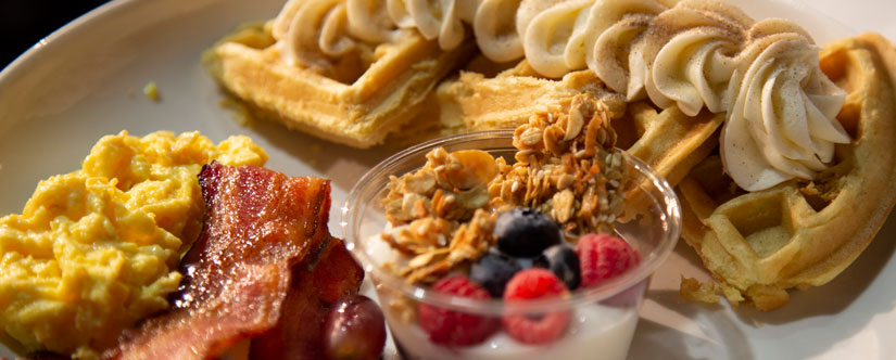 eggs and bacon, parfait cup with blueberries and rasberries, next to waffle on plate