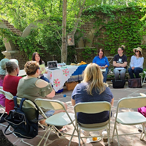 Adults in circle in outdoor garden discussing a book