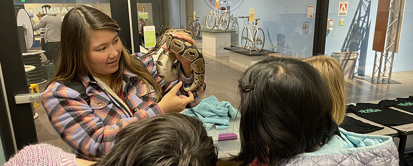 Woman holding large snake to 3 girls in front of her