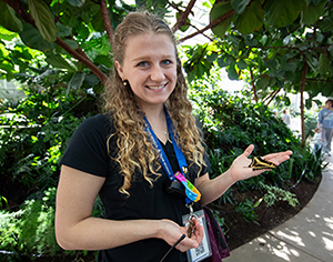 thanksgiving point explorer with long curly hair holding butterfly in butterfly biosphere conservatory